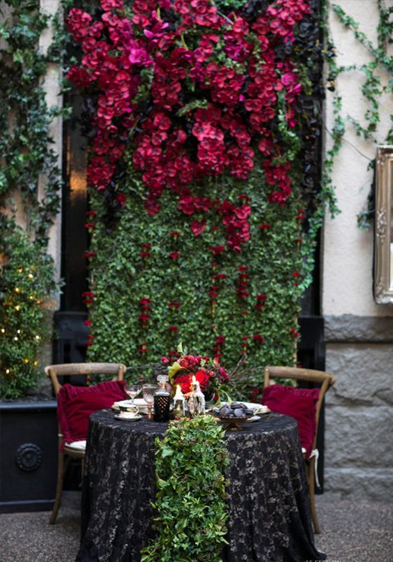 a living wall with lush black and burgundy blooms and a matching greenery runner on the table