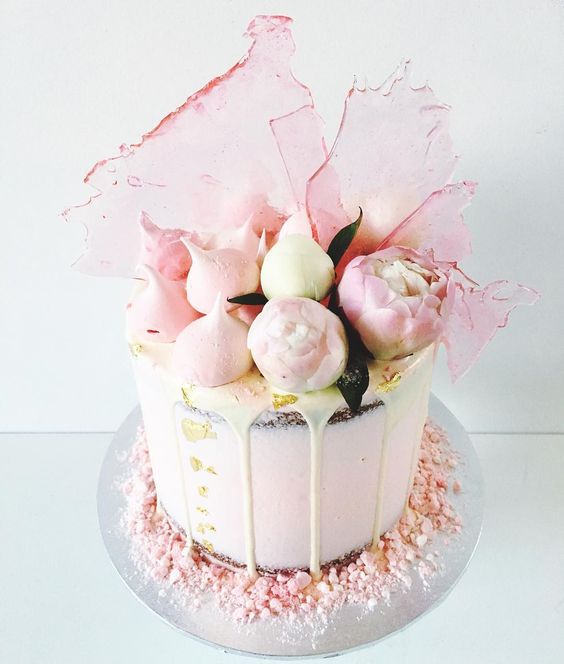 a semi-naked wedding cake with drip, blush blooms, blush meringues and pink sugar shards
