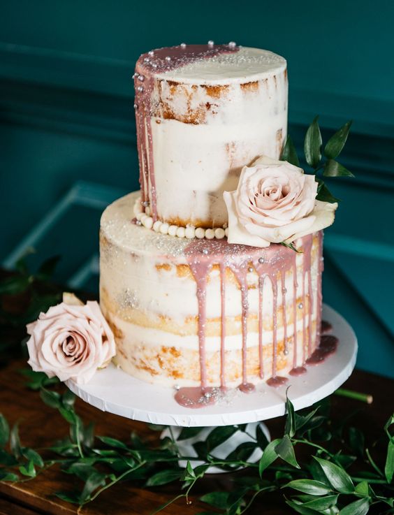 a naked wedding cake with dusty pink dripping, blush blooms and edible pearls for an elegant touch