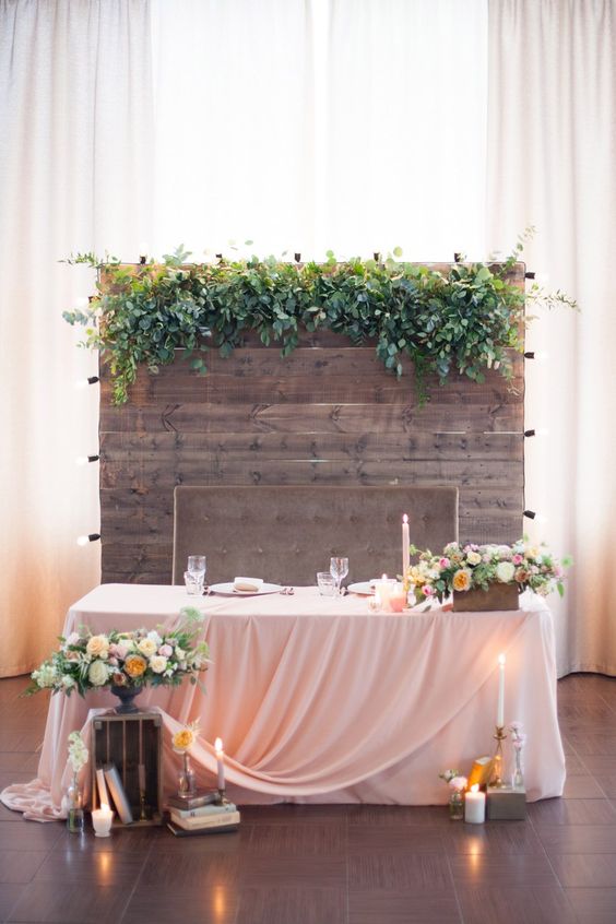 a barnwood backdrop with lush greneery on top and lights on its sides