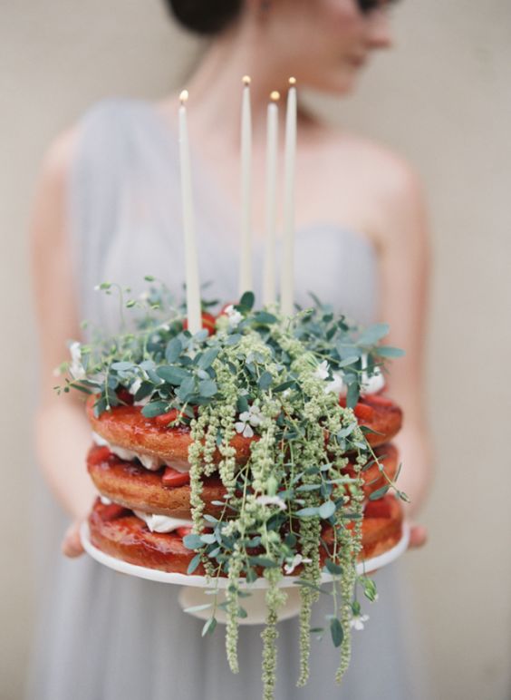 a naked wedding cake with strawberries, fresh greenery and candles on top