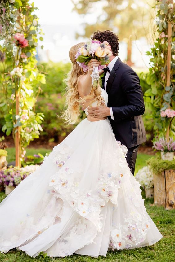 a spaghetti strap wedding dress with side cutouts and realistic flower appliques on the skirt