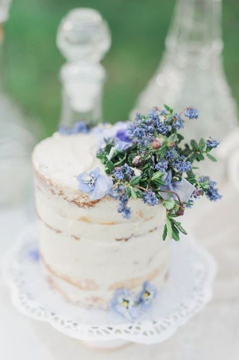 a semi-naked wedding cake decorated with blue flowers and foliage looks ethereal