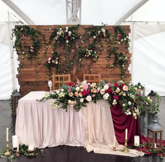 a wooden backdrop with greenery and lush blooms and matching ones on the table