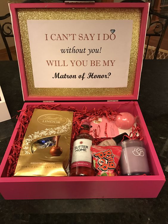 a pink box with a candle, a lip balm, some chocolate and a mini alcohol bottle
