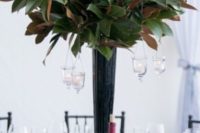 14 a tall black vase with magnolia leaves and some hanging candles as a centerpiece for a wedding
