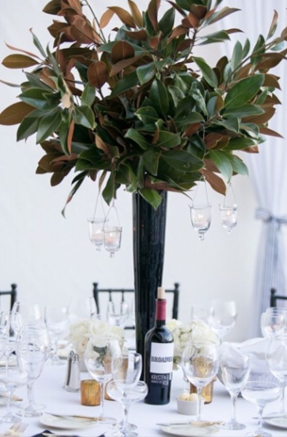 a tall black vase with magnolia leaves and some hanging candles as a centerpiece for a wedding