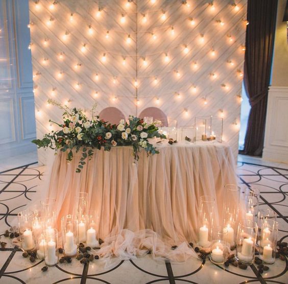 a draped blush fabric backdrop with lots of lights perfectly matches the table decor and looks cute