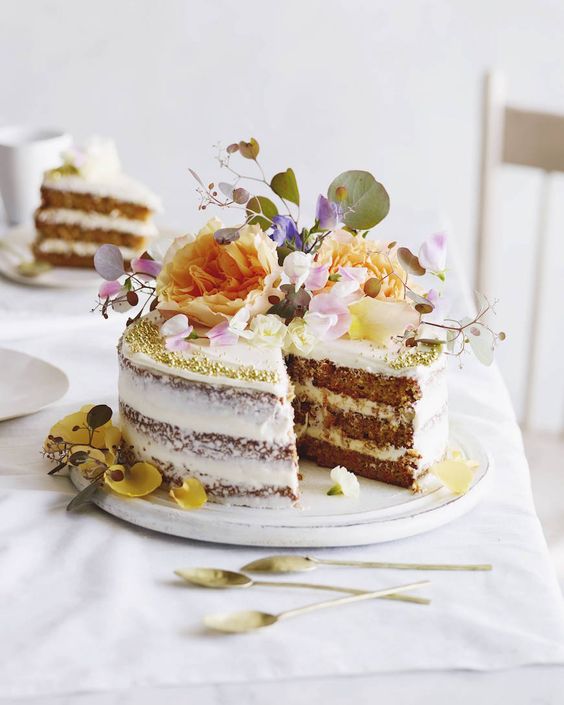 a naked wedding cake with gold glitter and lush blooms and foliage on top