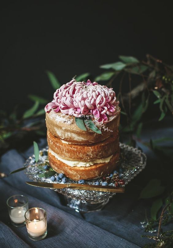 a tall yet small naked wedding cake topped with a single large bloom in pink looks elegant