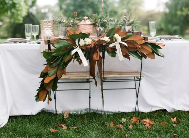 the couple's chairs decorated with magnolia leaves and ribbon bows