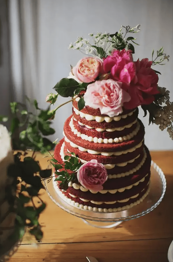 a beautiful naked red velvet wedding cake with pink and blush blooms, greenery and sugar pearls is a cool idea for a spring wedding