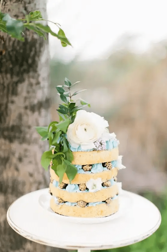 a boho naked wedding cake with blue cream, gilded blackberries, a large bloom and foliage
