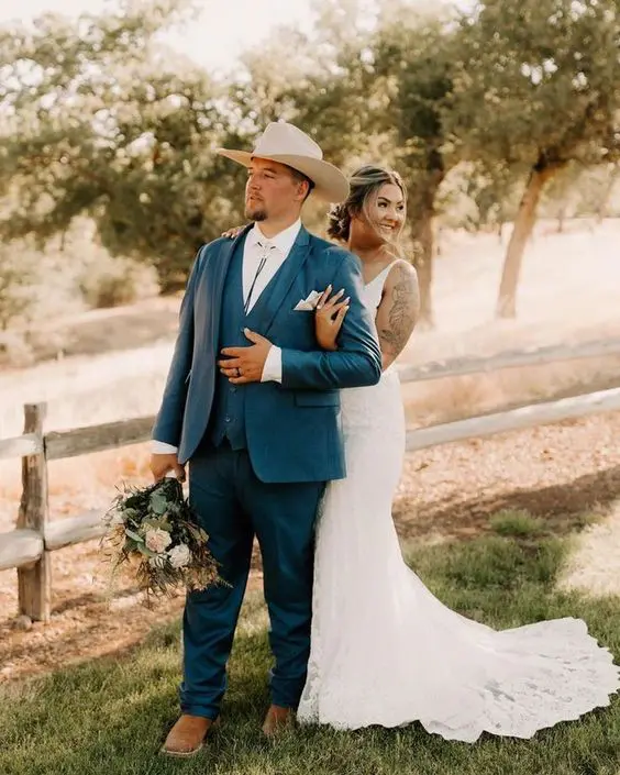 A catchy rustic groom's look with a navy three piece suit, a white shirt, a bolo tie and a neutral hat is cool
