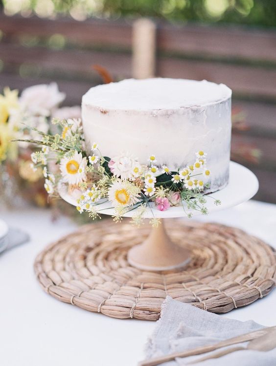 a classy naked wedding cake with some wildflowers and greenery on the side is a cool idea for a spring or summer wedding