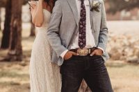a classy rustic groom’s look with a white shirt, a light blue blazer, navy jeans, a belt with a large buckle and a neutral hat