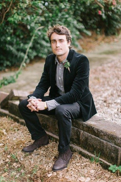 a dark informal groom's outfit with a grey shirt, a black velvet jacket, black pants and brown shoes