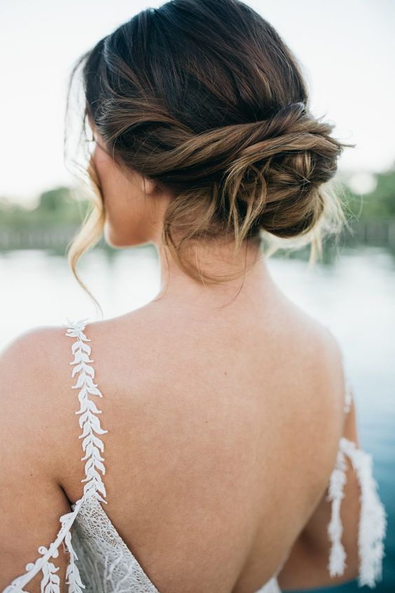 a messy and loose twisted low updo with some waves down is a cool idea for a wedding
