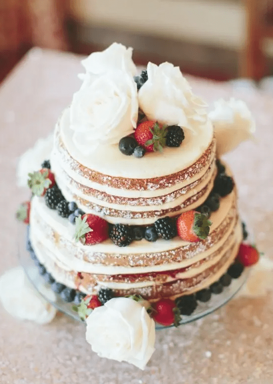 A mouth watering naked wedding cake with white blooms and fresh berries is a lovely dessert for a rustic wedding