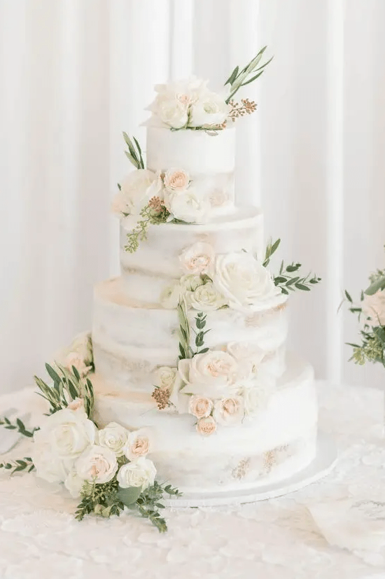 a naked four tier wedding cake with neutral and blush blooms and greenery is a very chic and delicious-looking idea