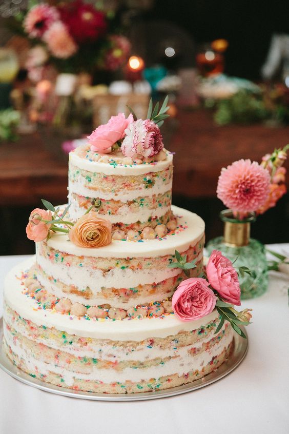 a naked funfetti wedding cake topped with bold blooms is a fun and cool idea for spring or summer