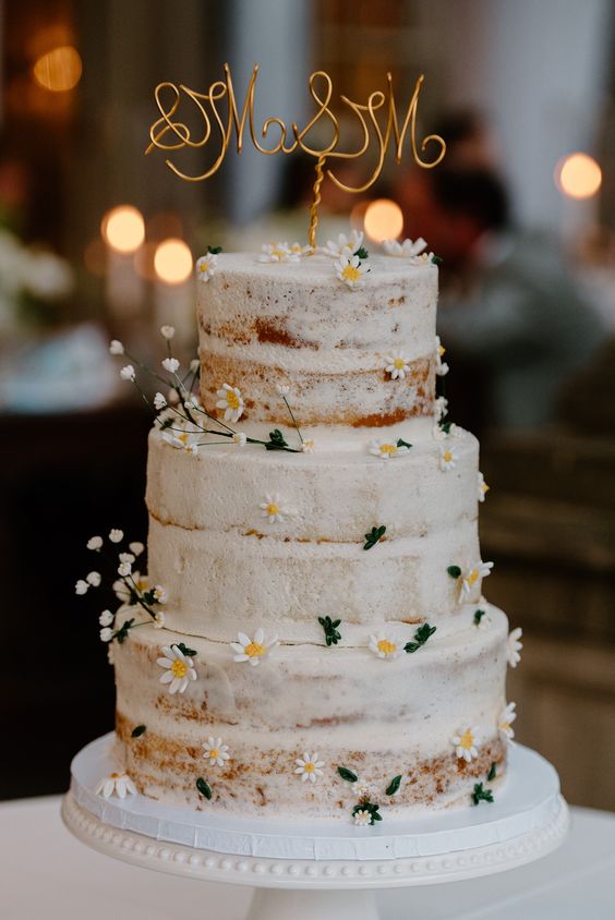 a naked wedding cake decorated with baby’s breath and chamomiles, with a calligraphy topper is a cool idea for a rustic wedding
