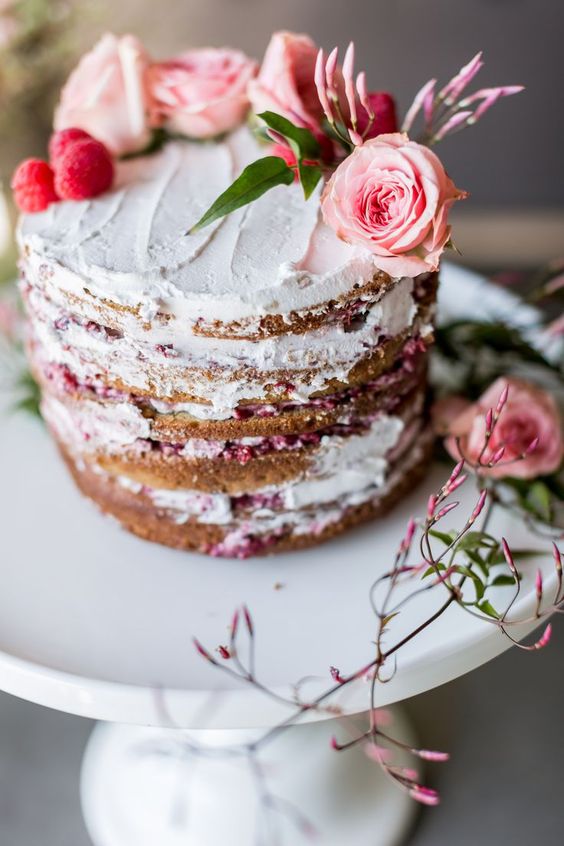 a naked wedding cake decorated with pink roses, raspberries and leaves is a cool idea for spring and summer