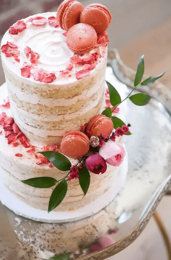 a naked wedding cake topped with bold coral petals and macarons, pink and purple blooms and greenery for a colorful spring wedding