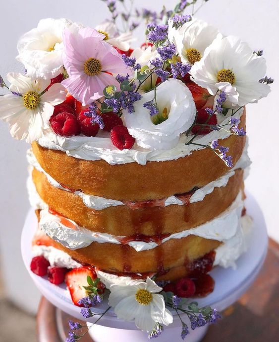 A naked wedding cake with berry drip, fresh raspberry and strawberry, white and pink blooms looks very spring like