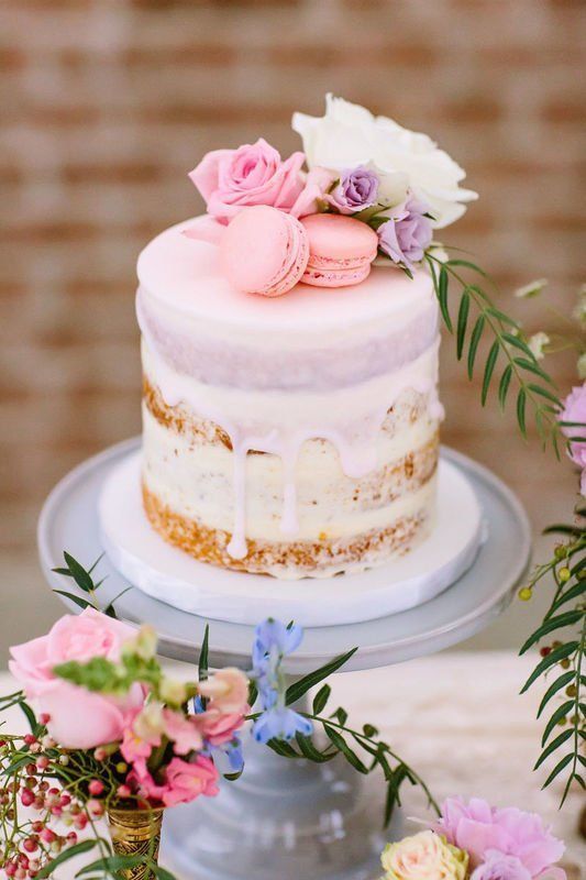 a naked wedding cake with creamy drip, pink macarons, white and pastel blooms is a beautiful cake for spring