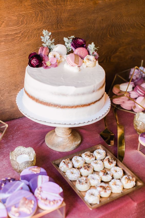 a naked wedding cake with pink macarons, purple ranunculus and greenery is a fantastic idea for spring