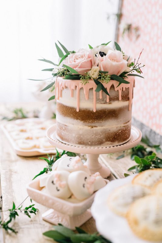 a naked wedding cake with pink roses and greenery on top and pink drip is a cool idea for a delicate spring wedding