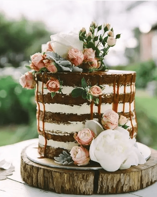 a naked wedidng cake with caramel drip, with pink and white blooms is amazing for summer or for spring