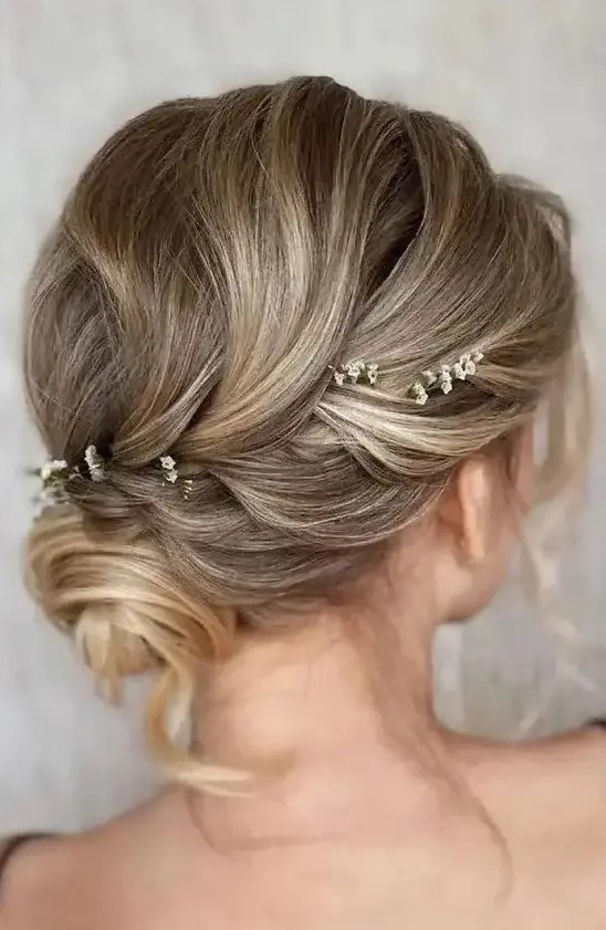 a refined and cool wedding updo with a volume on top, a small bun and some locks down plus some blooms tucked into the hair