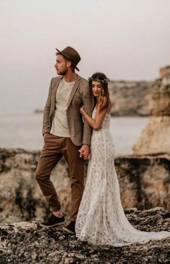 a relaxed groom's outfit with a neutral t-shirt, rust-colored pants, a grey blazer and a brown hat plus black shoes is cool for a boho wedding