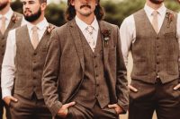 a rustic groom’s outfit with a brown three-piece pantsuit, a white shirt, a floral tie and a neutral hat is awesome