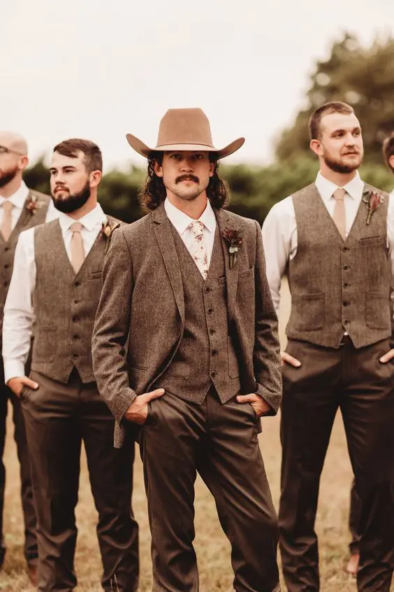 A rustic groom's outfit with a brown three piece pantsuit, a white shirt, a floral tie and a neutral hat is awesome