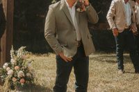 a rustic groom’s outfit with a white shirt, navy jeans, brown boots, a light green blazer and a neutral hat