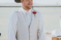 a rustic groom’s outfit with navy jeans, a white shirt, a neutral waistcoat, a striped tie and a brown hat