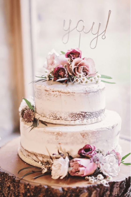 a rustic two-tier naked wedding cake with pastel and burgundy blooms and a calligraphy topper is a pretty idea