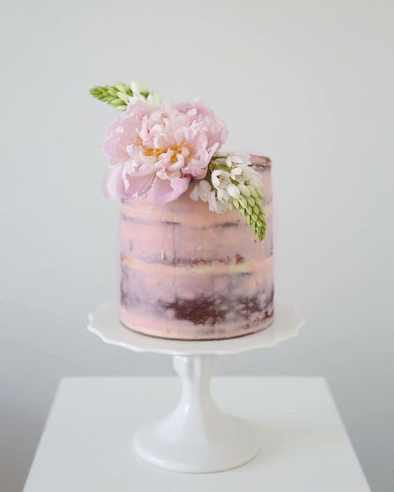 a semi-naked pink wedding cake topped with a large peony and some more blooms is a cool idea for a spring wedding