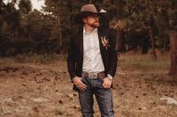 a stylish cowboy groom’s look with blue jeans, a white shirt, a black blazer, brown shoes and a hat