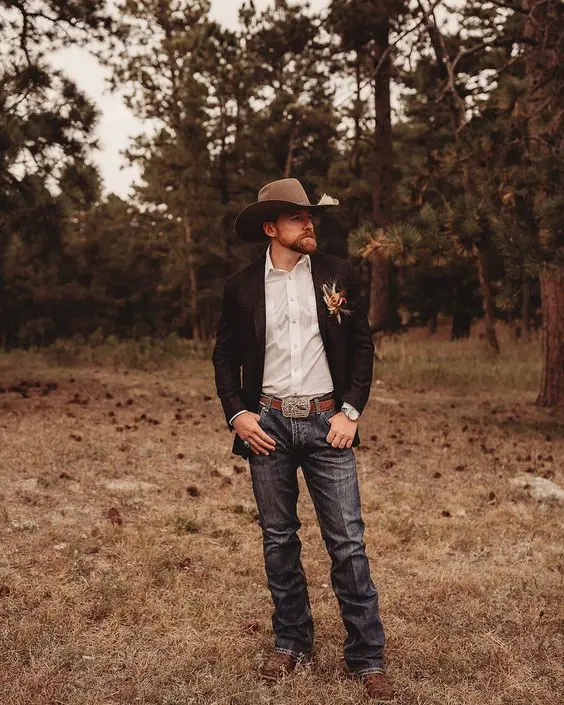 a stylish cowboy groom's look with blue jeans, a white shirt, a black blazer, brown shoes and a hat