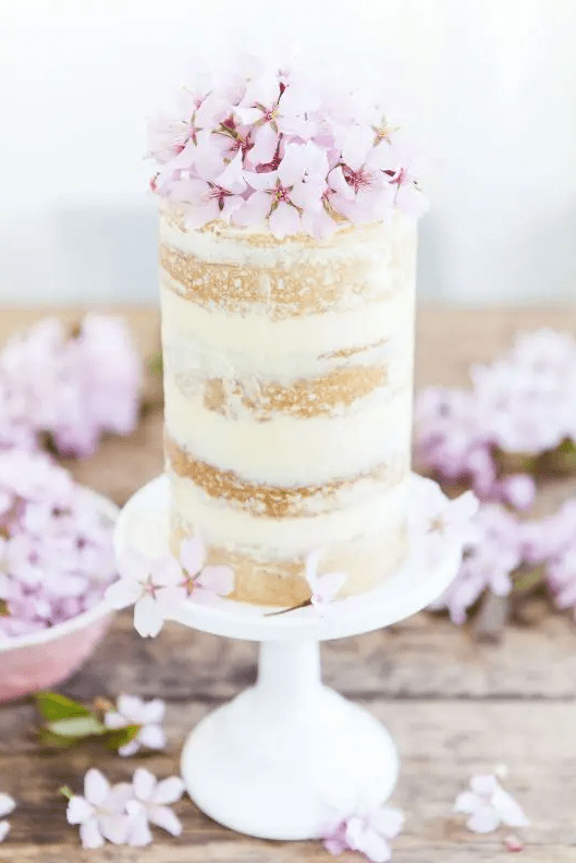 a tall naked wedding cake with tender pink blooms on top looks very chic and very romantic