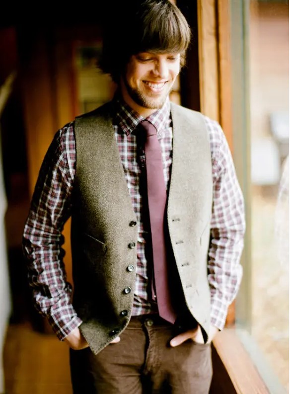 a very relaxed rustic groom's look with brown pants, a plaid shirt, a purple tie and a grey waistcoat
