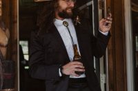 a western groom’s outfit with a black suit, a white shirt, a bolo tie and a neutral hat is a cool idea for a boho wedding, too