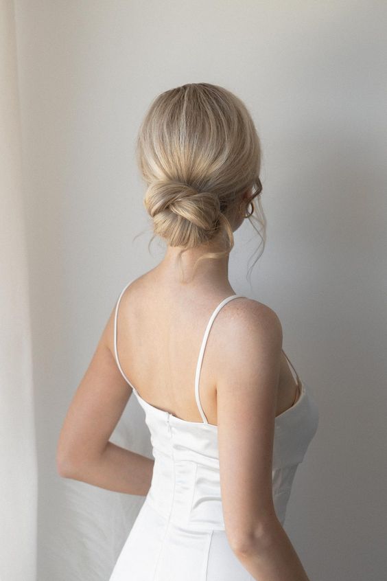 a woven low bun wiht a sleek yet dimensional top and waves down is a stylish and elegant idea for a wedding