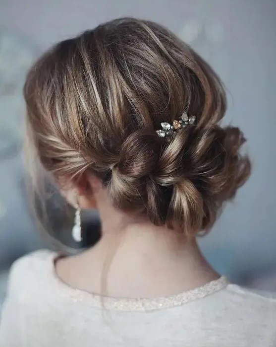 an elegant updo with a large braided element, a bump and a rhinestone hairpiece for a romantic feel
