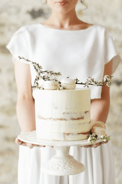 an ethereal white semi naked wedding cake topped with macarons and flowers is amazing for a spring wedding