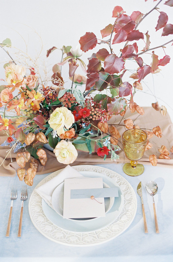 The wedding table setting was done with powder blue and light brown textiles, amber glasses and lush florals with fall leaves